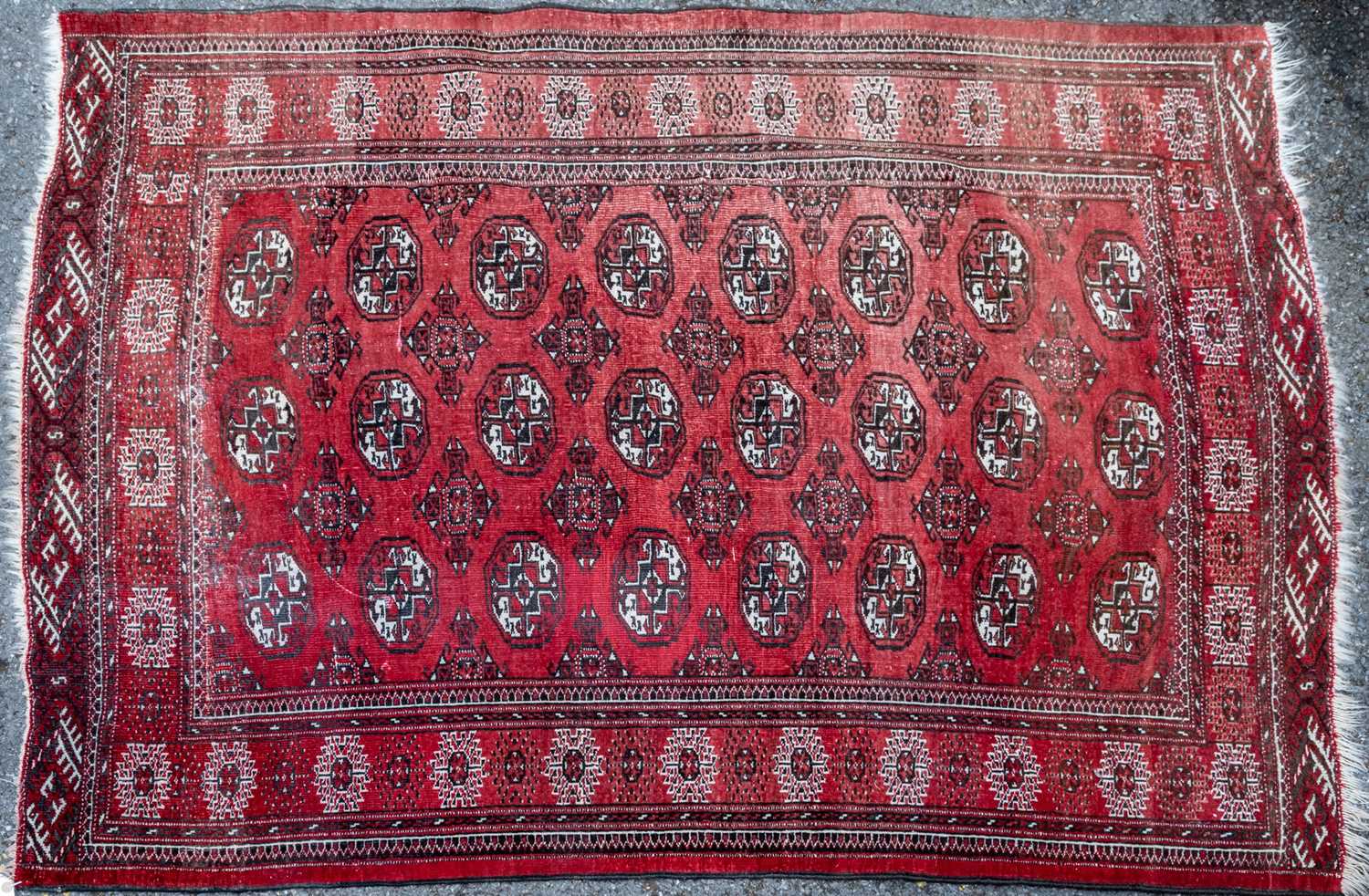 A red ground rug with all over geometric shapes within a brown and black banded border, 130cm x