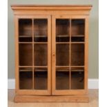 A pine bookcase, with a pair of glazed doors over shelved interior, on plinth base, 105cm wide x