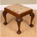 A Georgian style walnut framed stool with an embroidered inset seat, cabriole legs and claw and ball