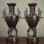 A pair of Japanese bronze vases with floral and foliate decoration, stylised bird handles on triform