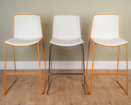 A pair of bar chairs with white plastic seats and orange edges, on orange painted metal frame