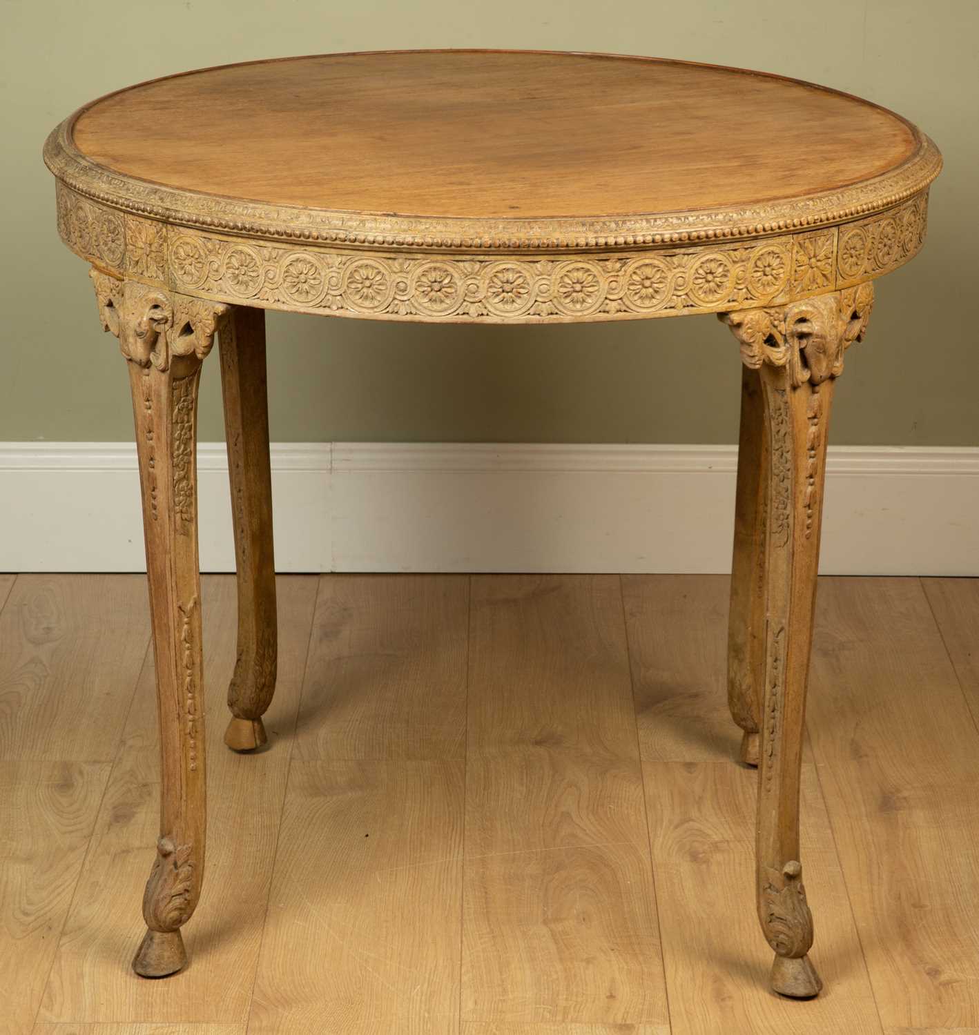 A circular Adam style occasional table with carved wooden edge, rams mask ornament and the legs