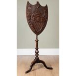 A 19th century mahogany pole screen, the shield shaped carved screen decorated with a heraldic