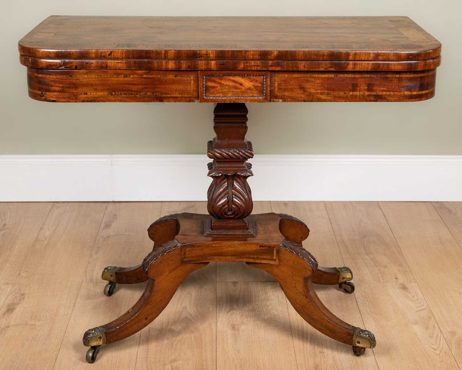 A George IV mahogany foldover card table with rosewood cross banded top, carved support and four