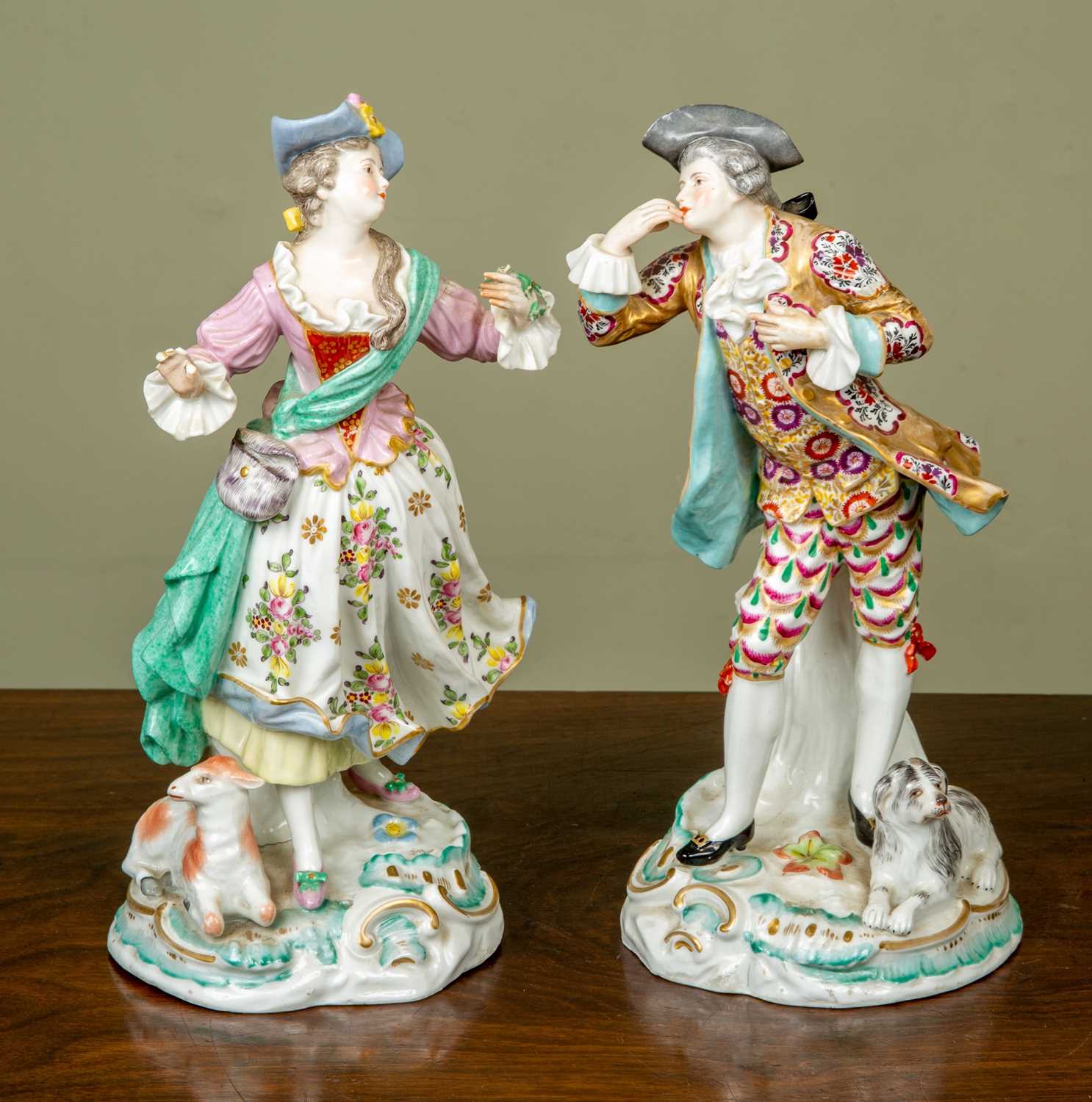 A pair of antique figurines depicting a gentleman and his belle, the gentleman with a dog resting at