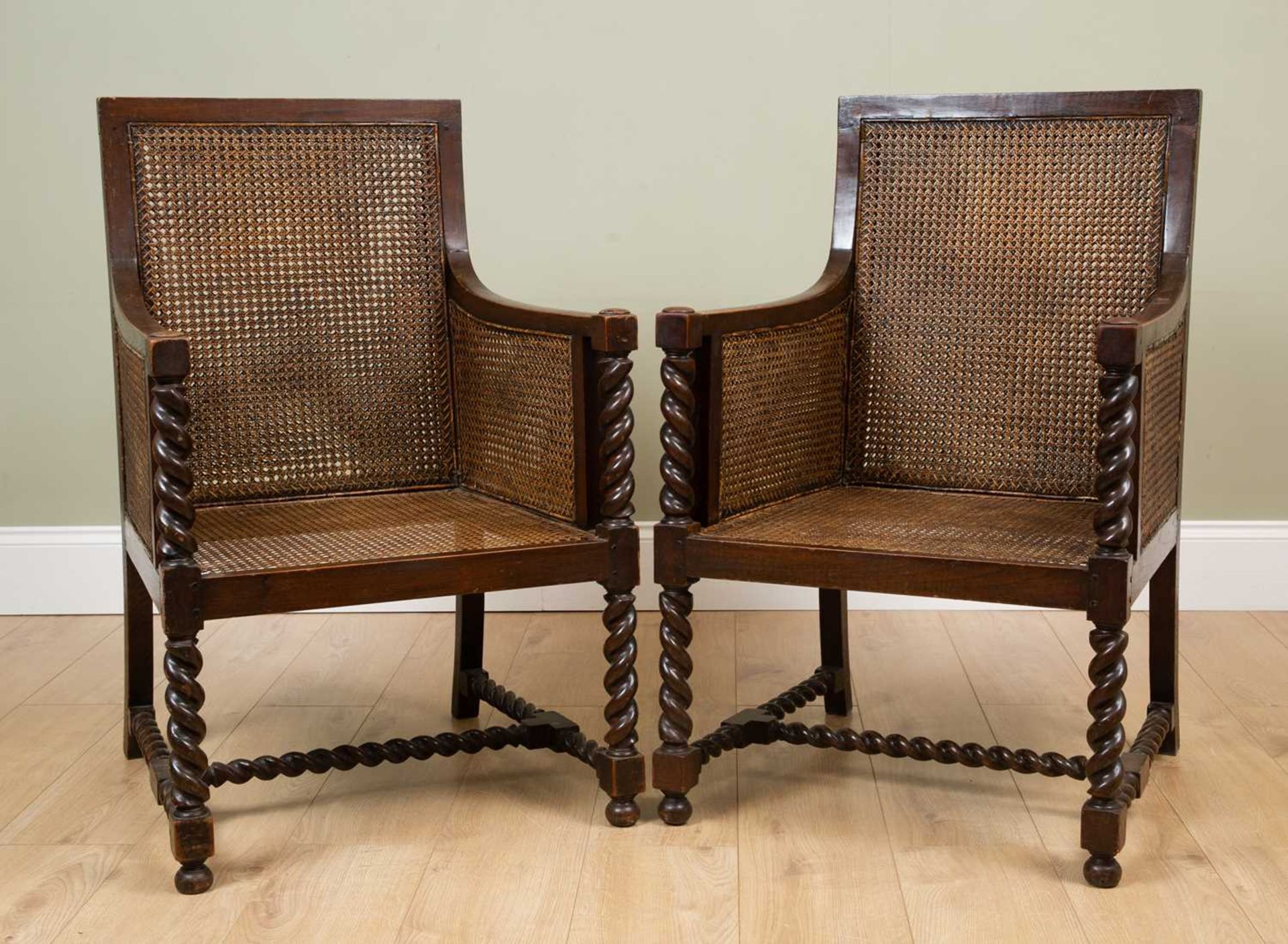 A pair of early 20th century oak framed Bergere armchairs with double caned backs and sides and with