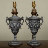 A pair of continental spelter oil lamps of vase form, decorated with putti, later converted for