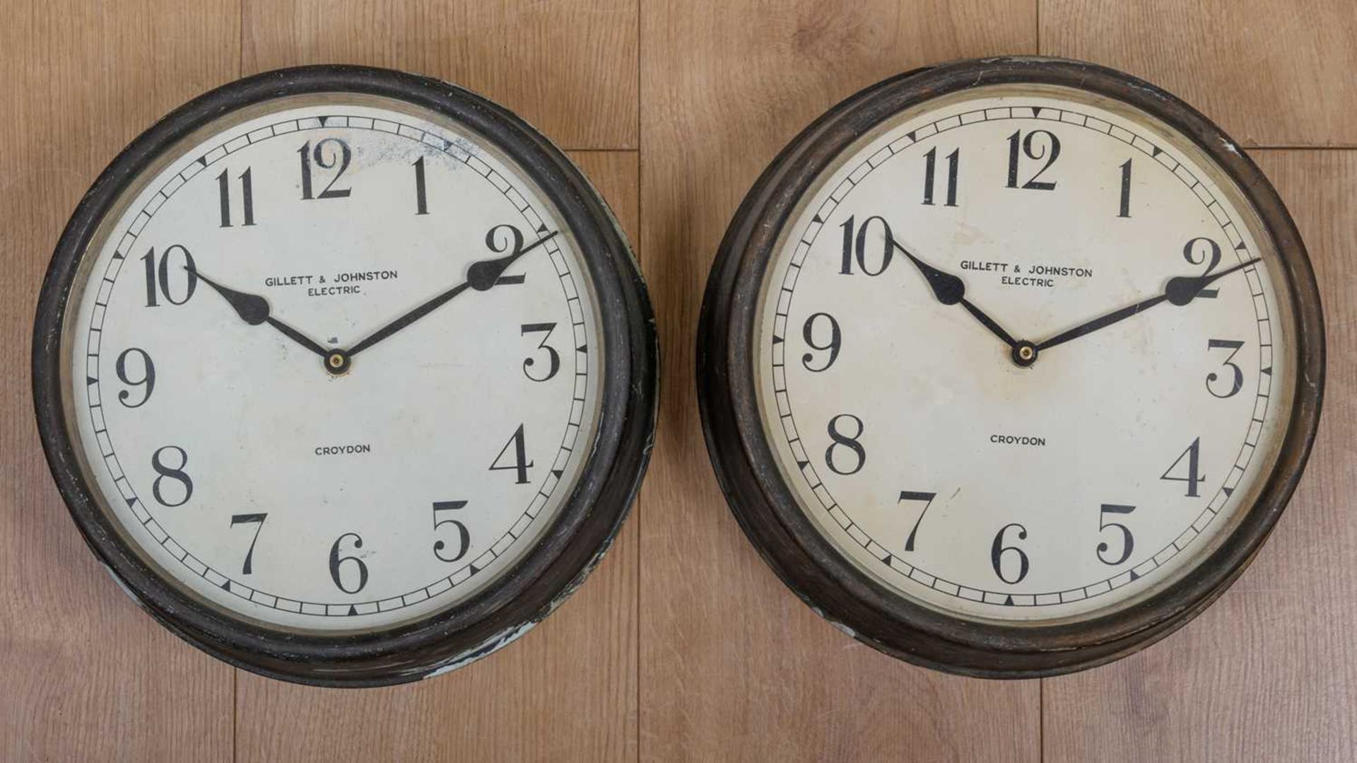 Two Gillett & Johnston electric wall clocks, the cases in bronzed tin with Arabic numerals to the