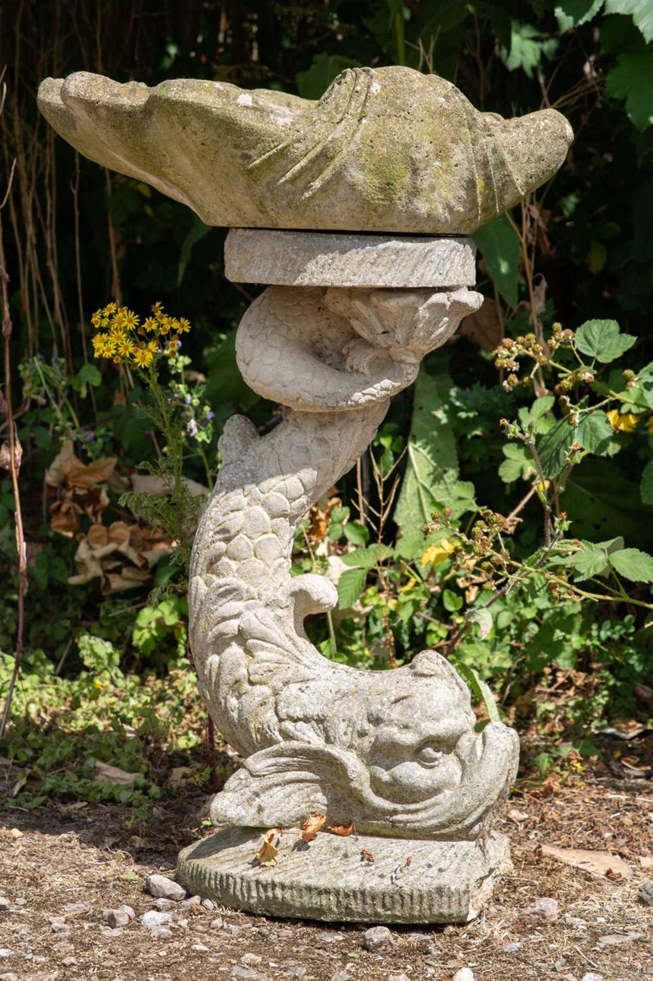 A cast reconstituted stone bird bath in the form of a shell supported by a dolphin, 52cm wide x 76cm