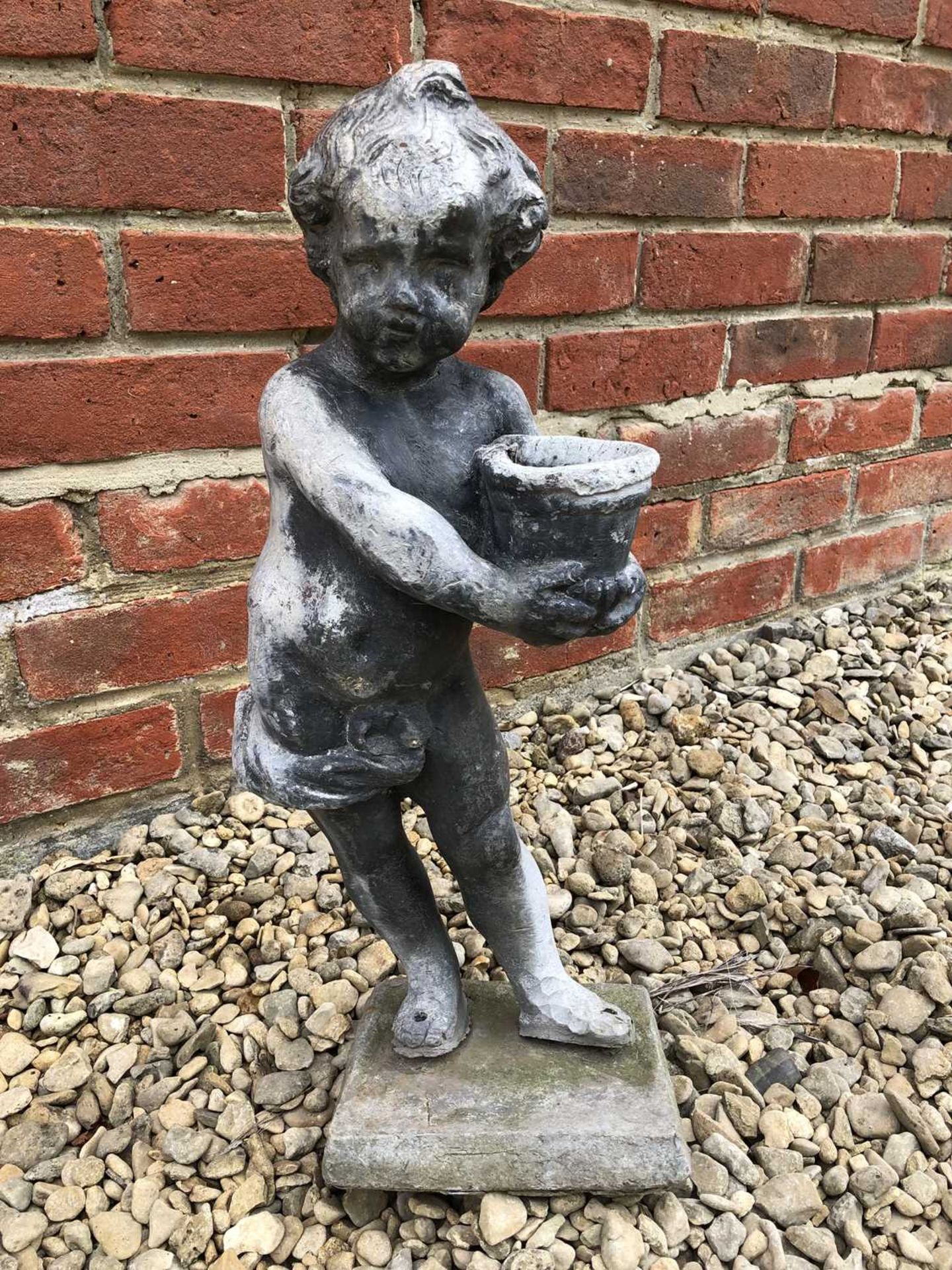 An antique lead putti in a standing pose with a basket, on a square plinth, 20cm wide x overall 52cm
