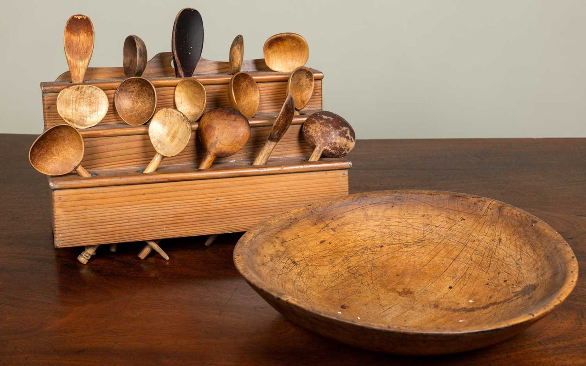An antique sycamore dairy bowl, 37.5cm diameter; together with a pine spoon rack with a collection