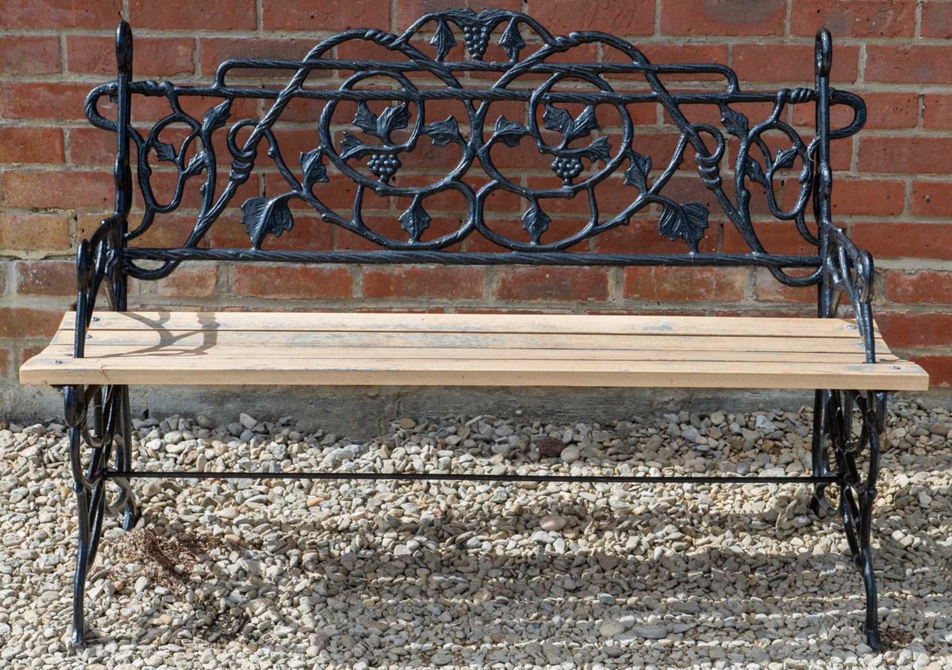 A cast iron garden bench with a wooden slatted seat, back decorated with vine and grape detailing,