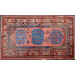 A Khotan long red ground rug with three central oval motifs on a floral central field and within a