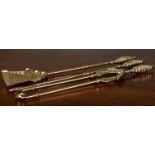 A set of three Edwardian brass fire irons with decoratively cast handles and pressed shovel blade,