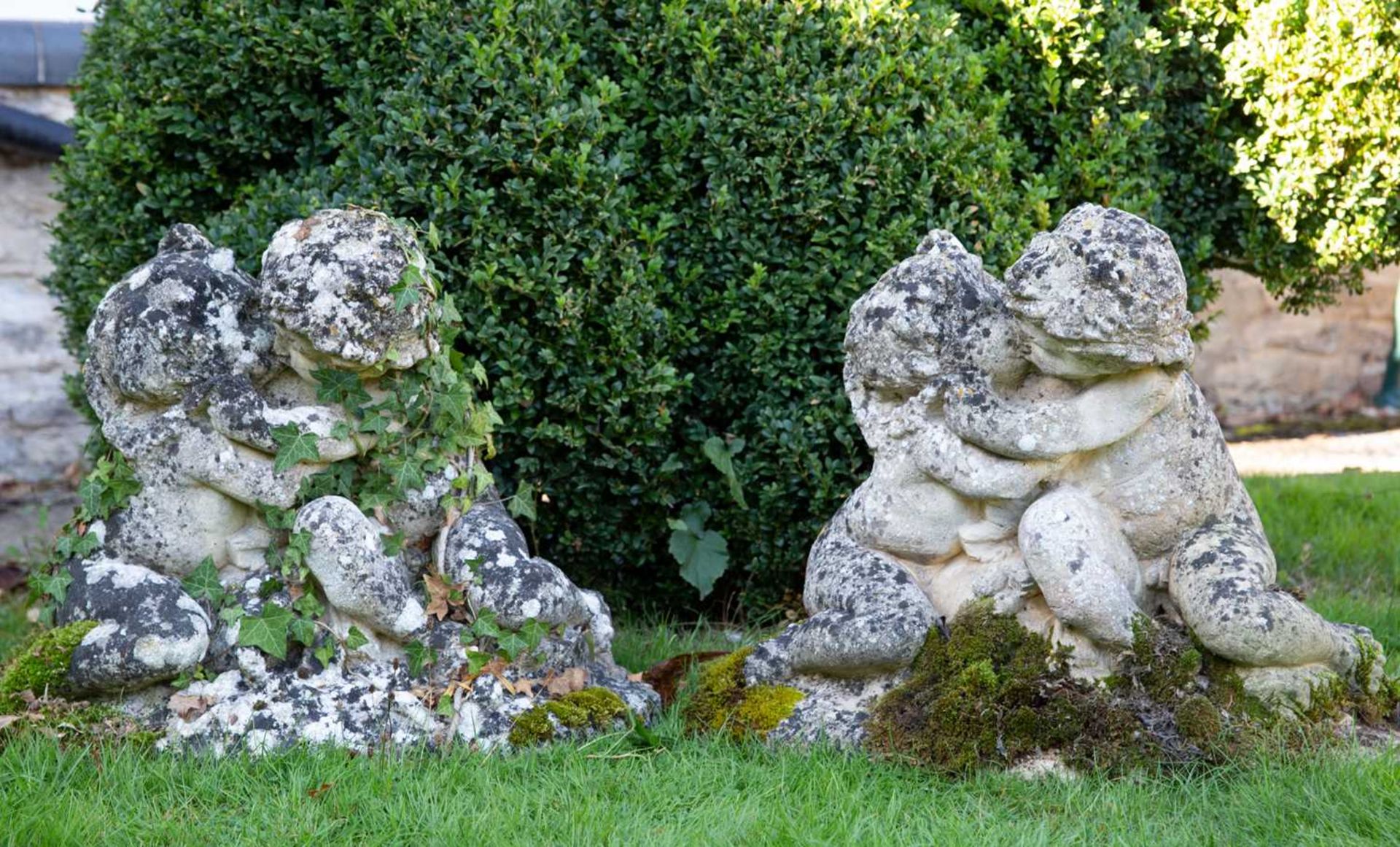 Two cast reconstituted stone groups of putti, each 64cm wide x 48cm high (2)Qty: 2In weathered