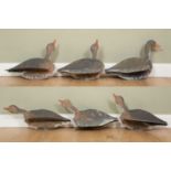 A collection of five painted plywood decoy geese, with adjustable necks and pegs beneath, each