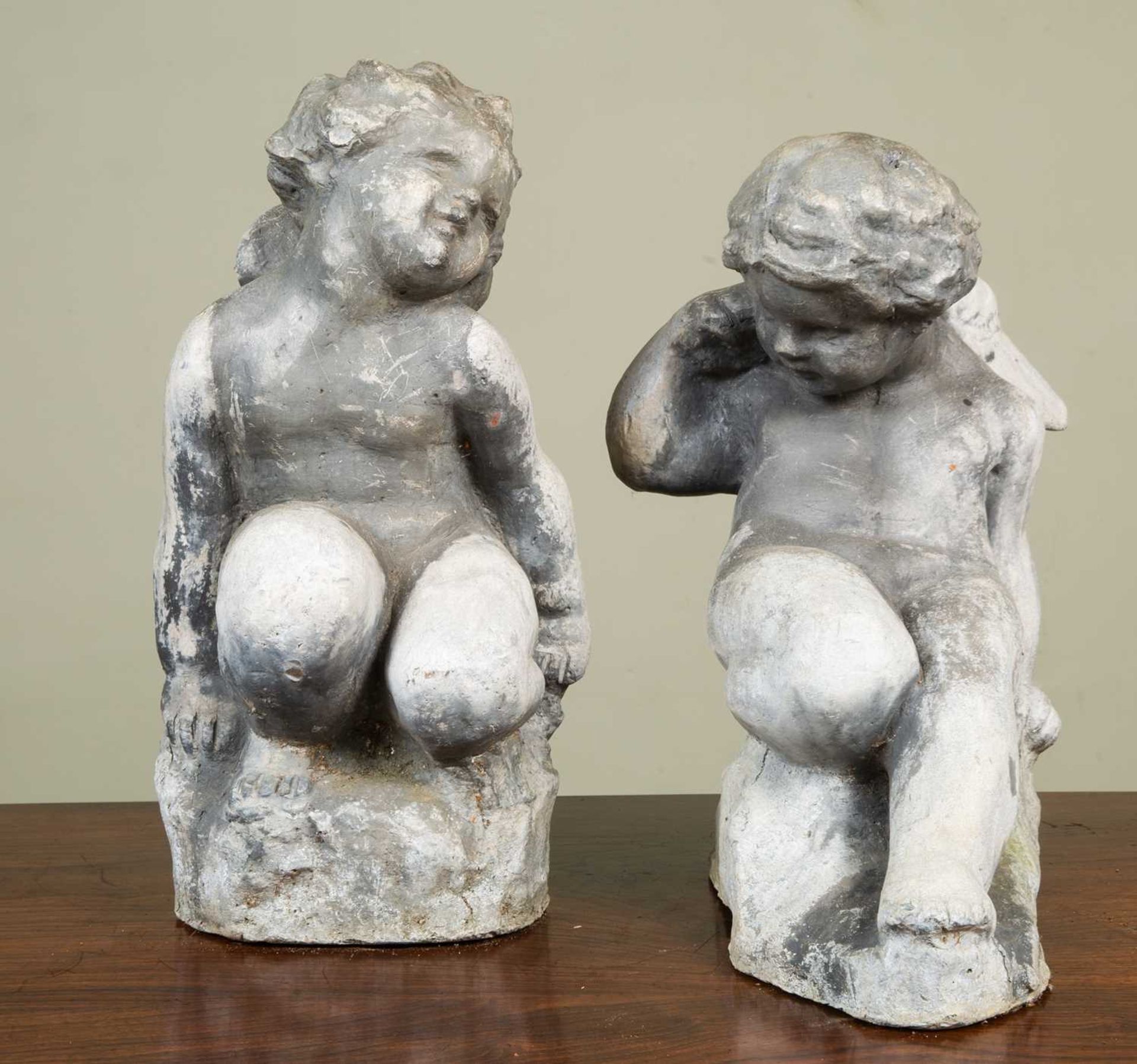 Two antique lead cherubs each in a playful pose, both approximately 36cm in height x 20cm wideSome