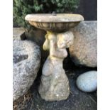 A composite stone bird bath fountain, modelled as a putto holding aloft the shallow, circular