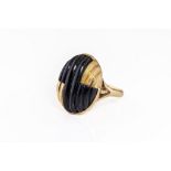 An 18ct gold and carved onyx ring, 1980s, the oval ring in assymetric reeded gold and carved onyx,