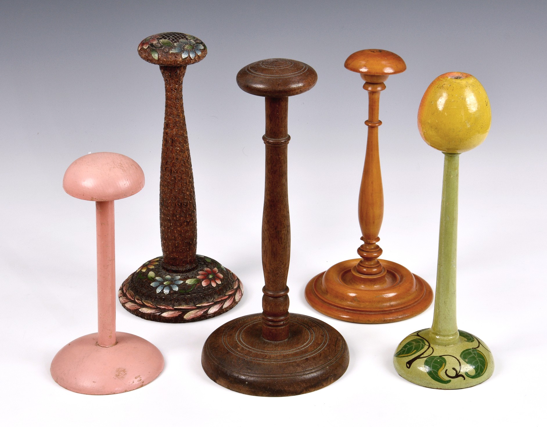 A collection of five wooden wig stands, to include a turned box wood version, one with an apple