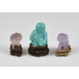 A miniature Chinese carved turquoise figure, sitting upon a carved hardwood stand, 2 ¼in. (5.8cm.)