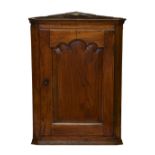 A George III oak corner cupboard, with cavetto cornice, over a shaped panelled door enclosing