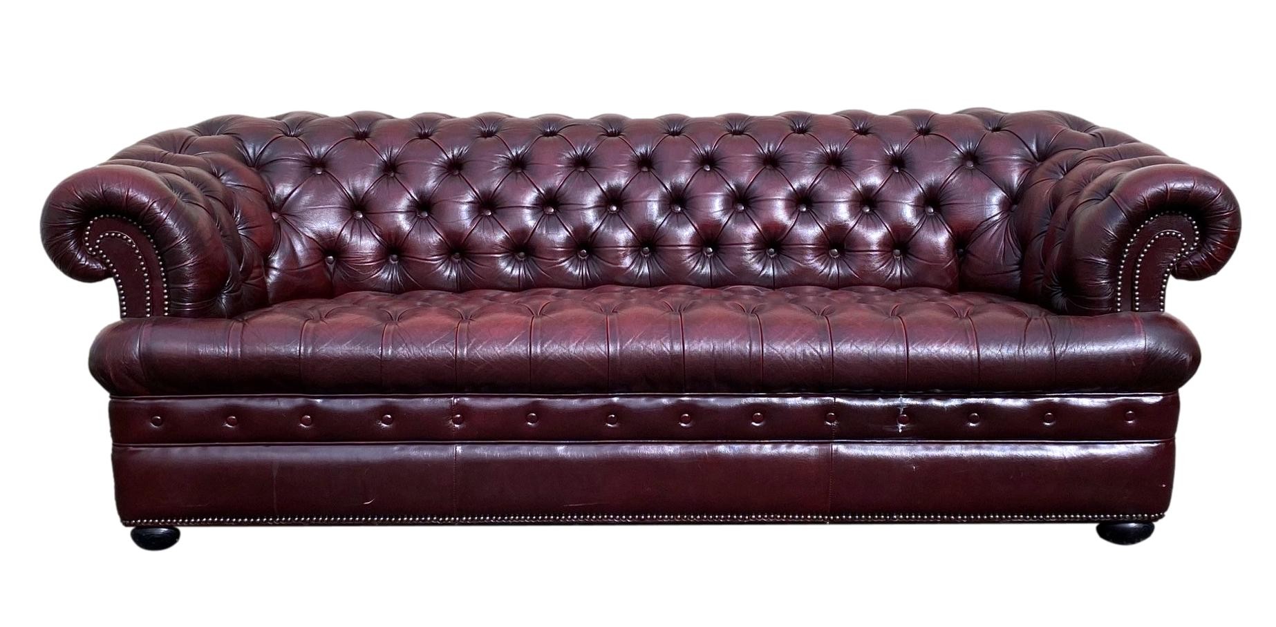 A modern leather Chesterfield sofa in deep red buttoned leather with studded scroll arms