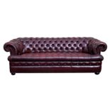 A modern leather Chesterfield sofa in deep red buttoned leather with studded scroll arms