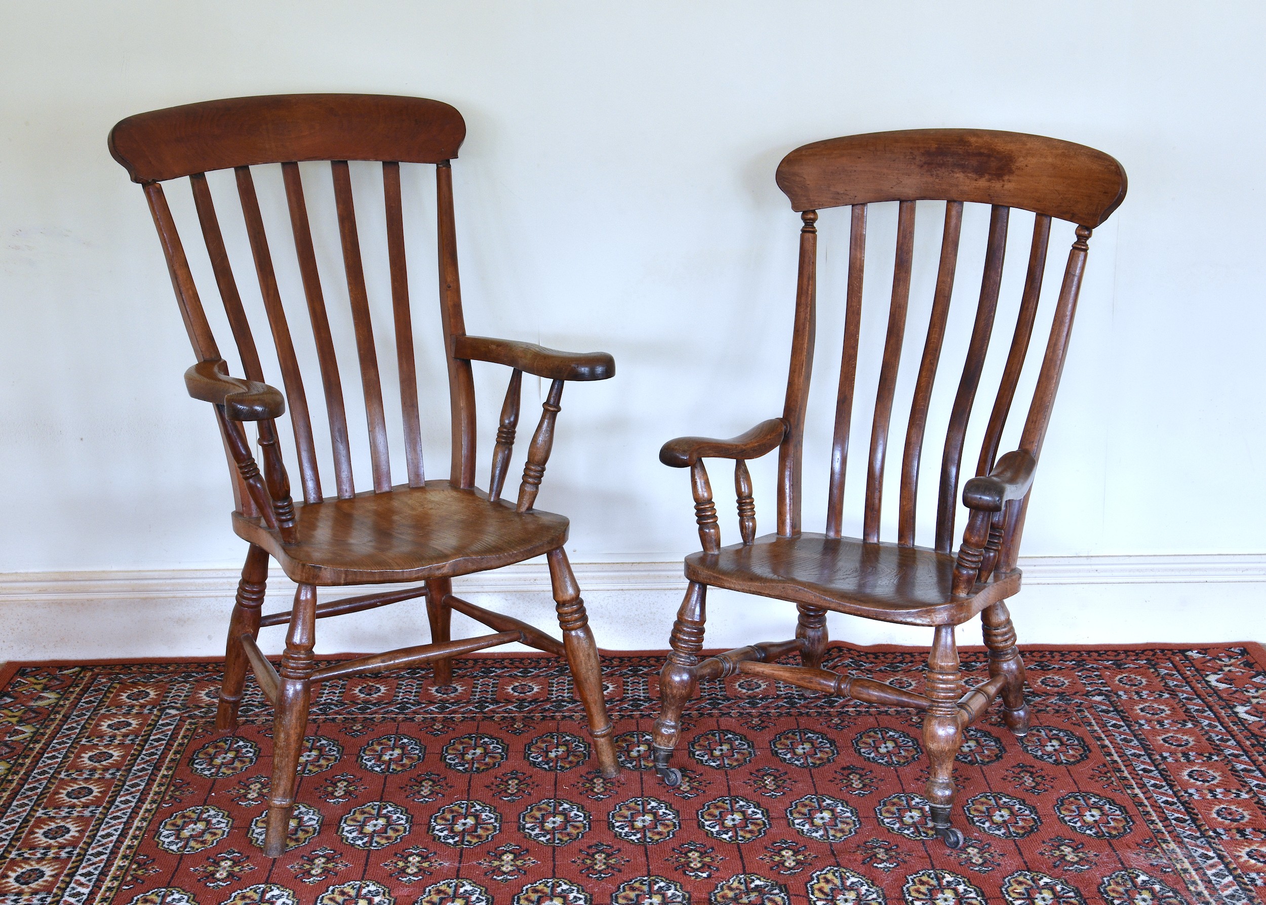 Two Victorian beech and oak lath back kitchen armchairs, with solid seats and shaped arms, on turned