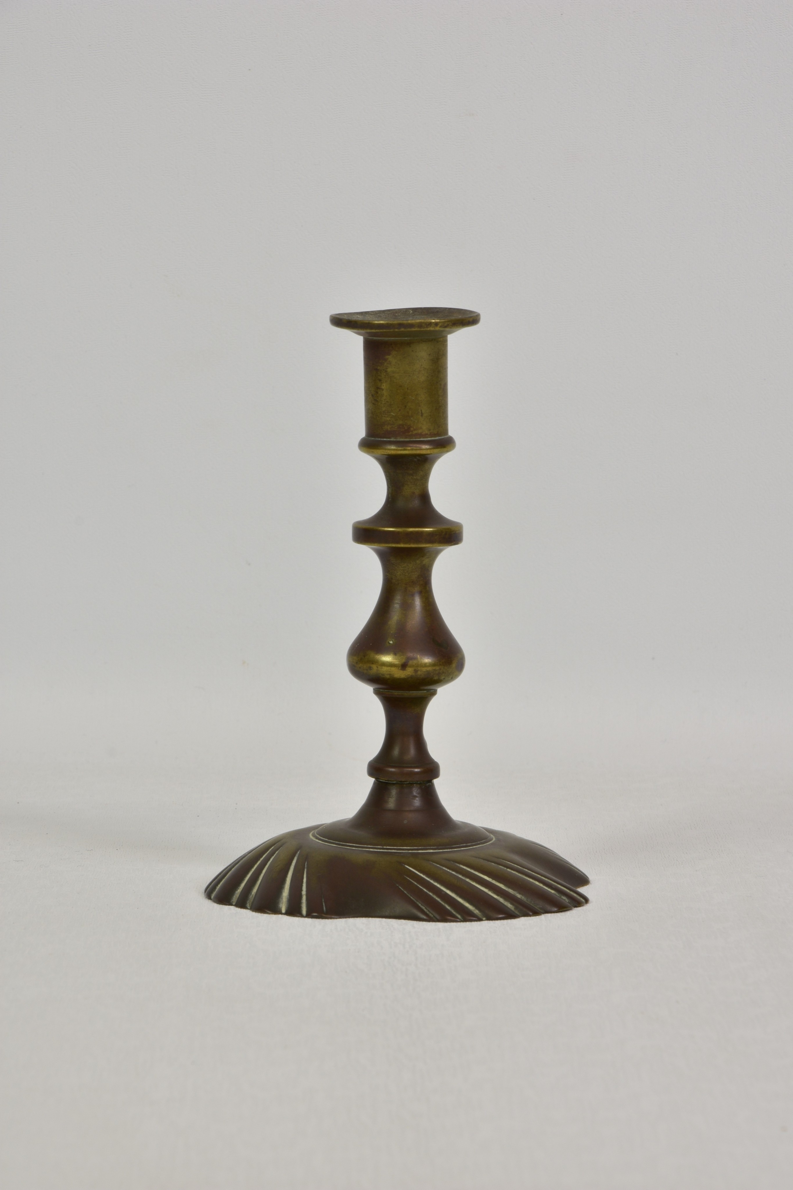 An early to mid 18th century brass candlestick, on a knopped and baluster stem, with a shallow,