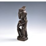 Tribal art - A carved wooden ancestor figure, Indonesia, probably Leti Islands, seated with arms