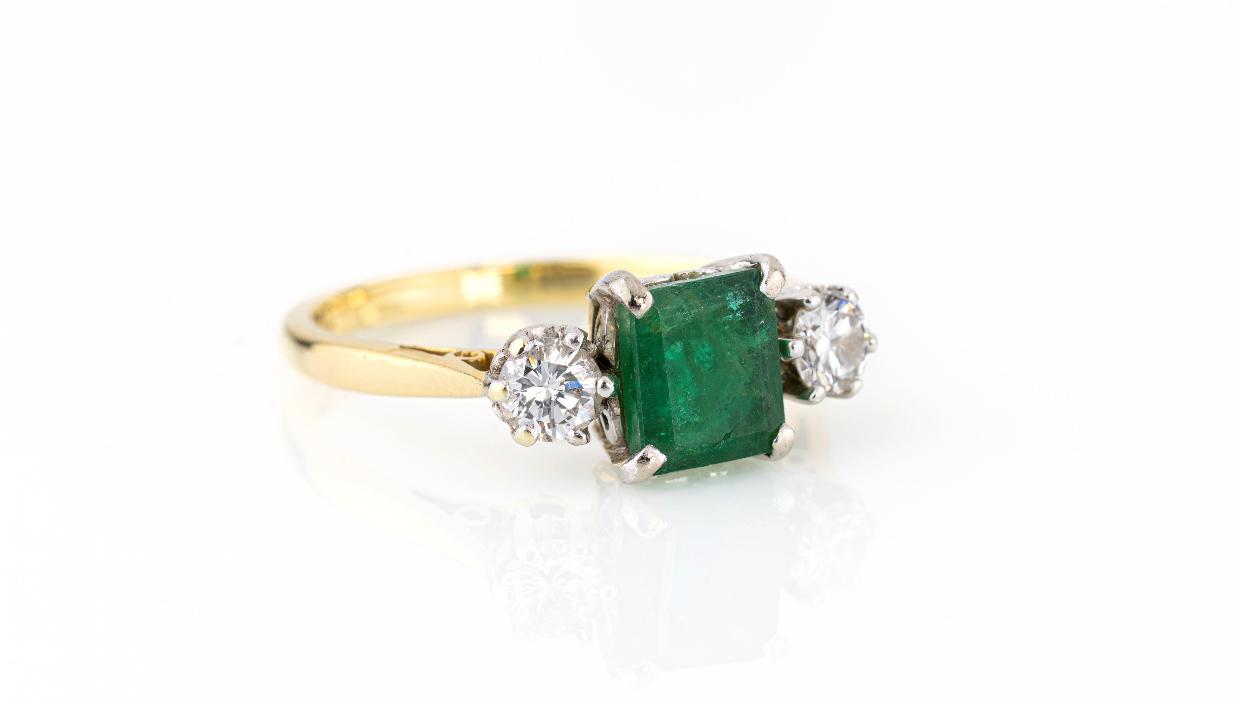 An 18ct yellow gold, emerald and diamond three stone ring, the central 6.75 x 6mm. emerald flanked