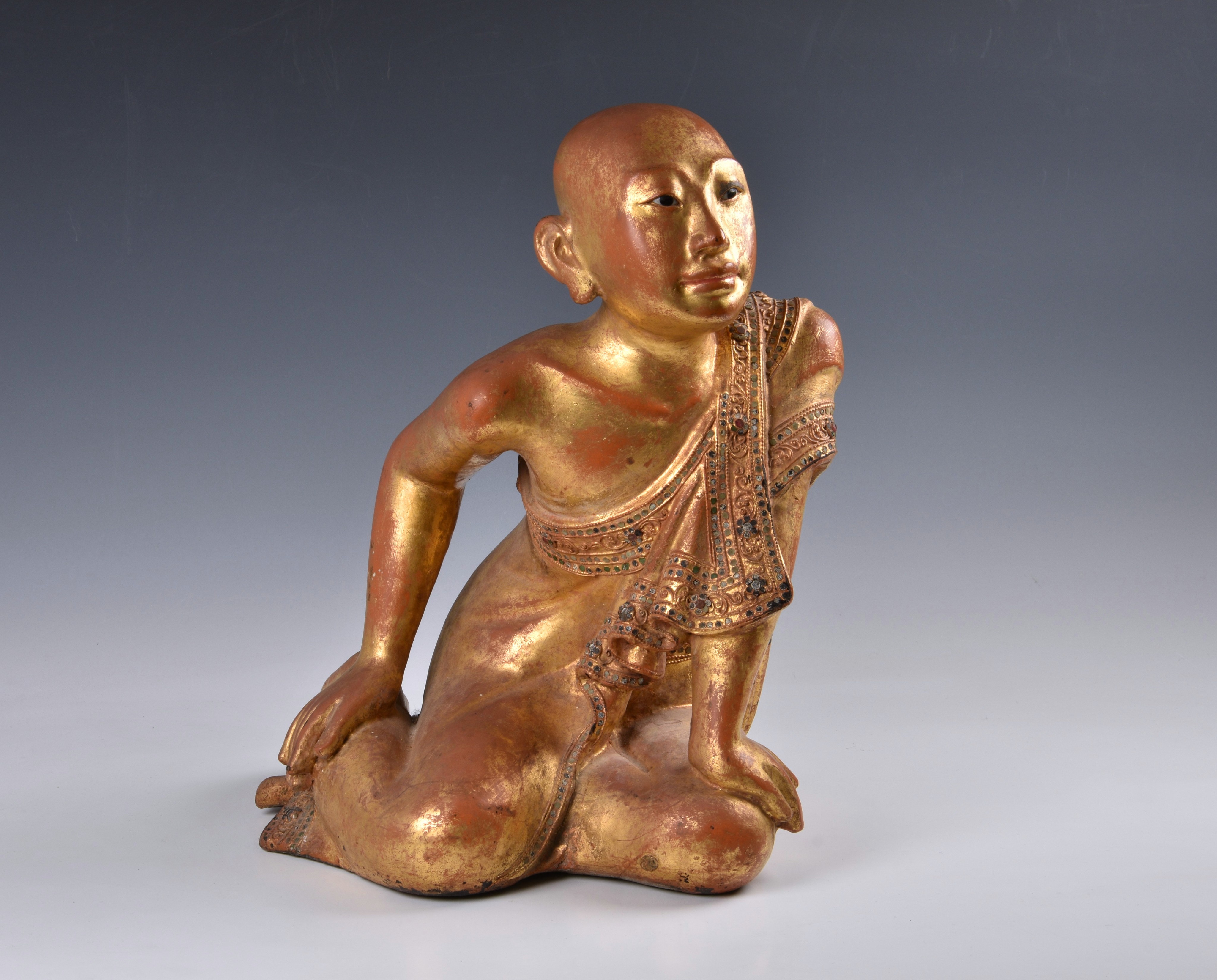 A Burmese Mandalay carved, lacquered and jewelled gilt wood figure of a seated monk, probably late