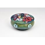 A Moorcroft Pottery powder bowl and cover, 'Frilled and Slipper Orchid' pattern, on a shaded blue-