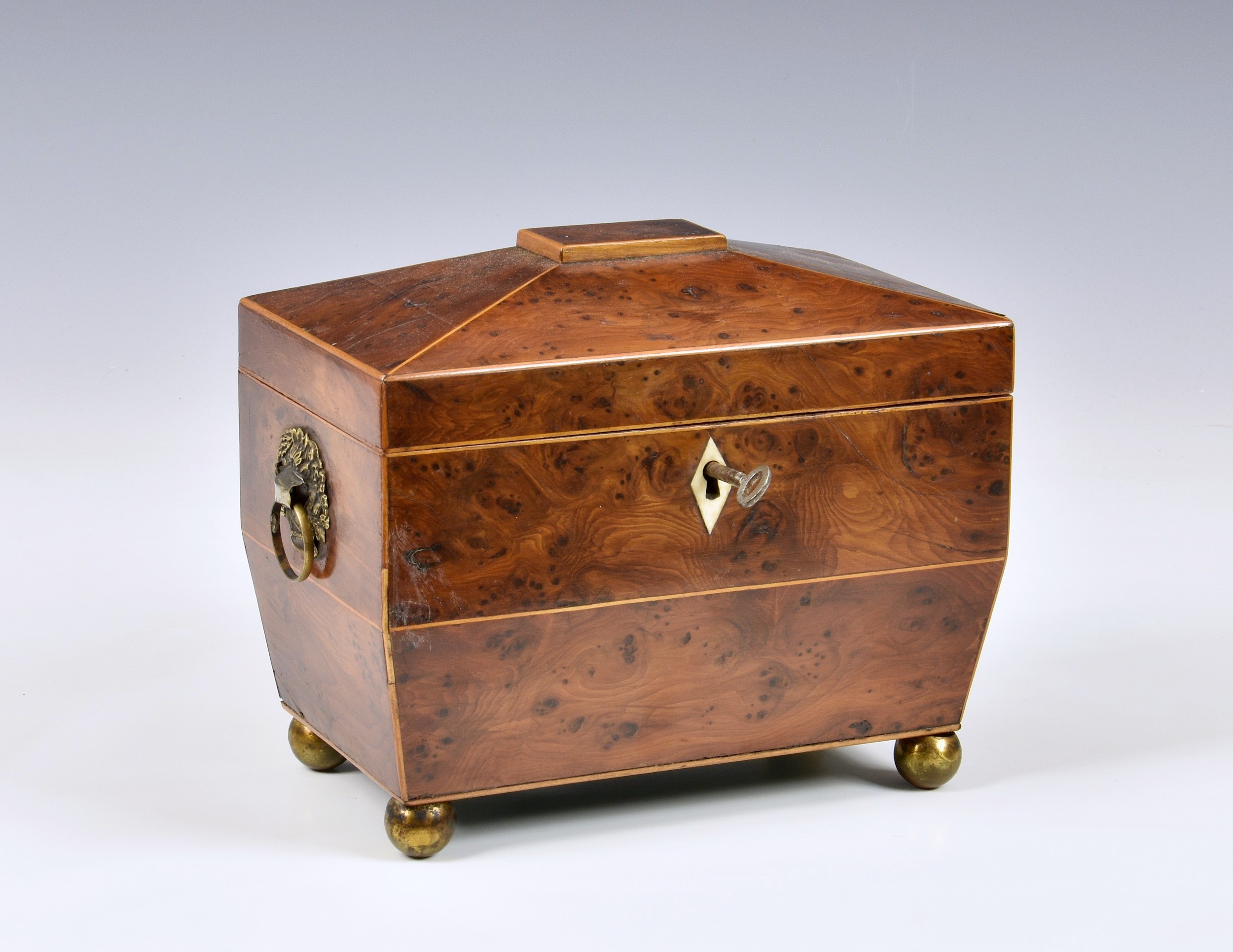 A George III burr yew tea caddy, of sarcophagus form with string banding, loose ring handles to