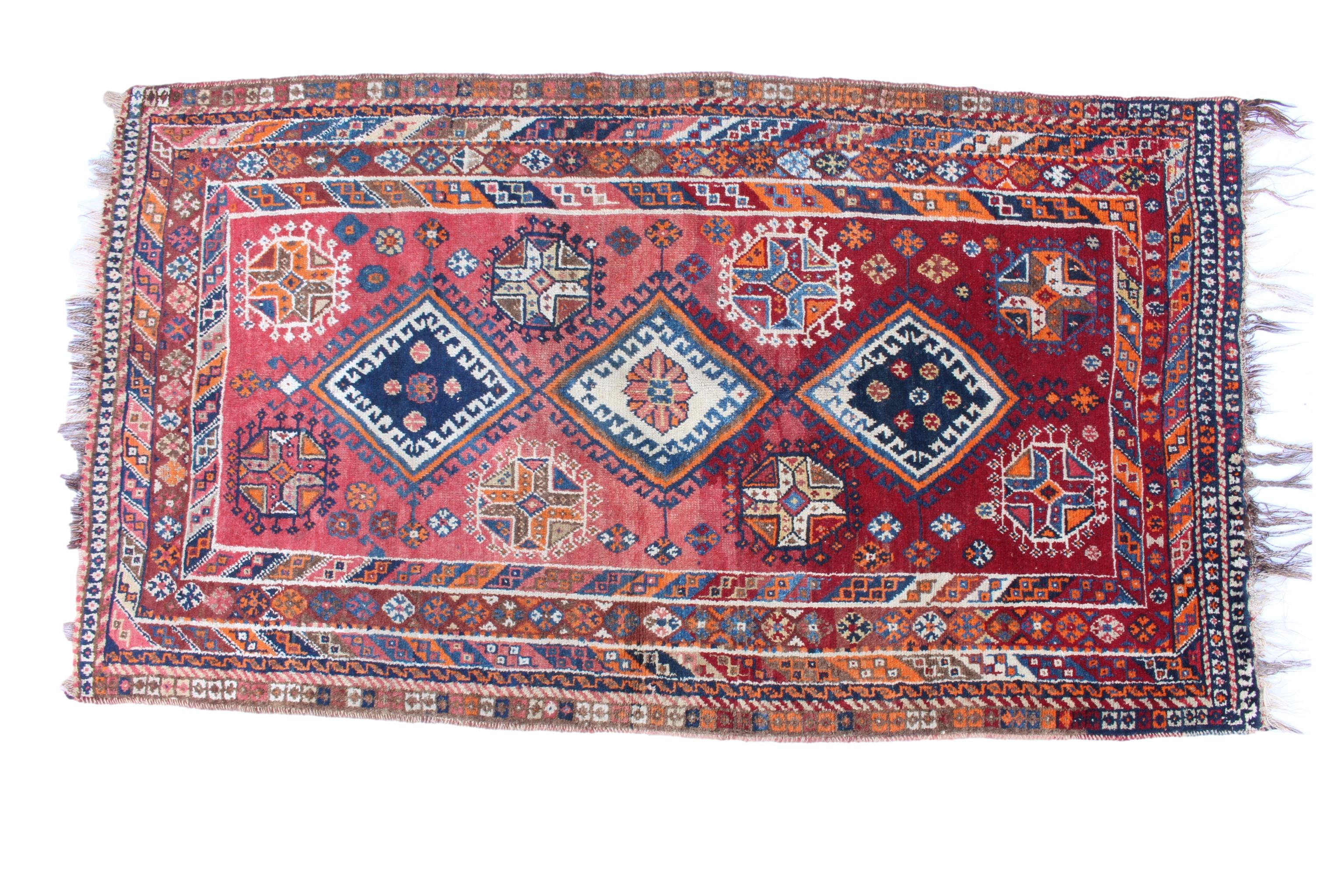 A Persian style rug, on red ground, with three hooked diamond medallions and florette and gul