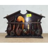 An oak pipe rack with a selection of carved and other pipes.