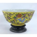 A Chinese yellow ground bowl with wooden stand, decorated to exterior with bats in different