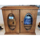 An oak double door smoker's cabinet with composition handles, ceramic tobacco jar and pipes