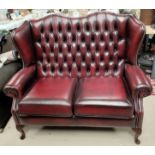 A 2 seater wing back settee in deeply buttoned oxblood hide