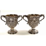 A hallmarked silver pair of Irish cast loving cups with twin handles, extensive relief decoration of