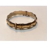 A 9ct gold bangle of shaped bamboo form with safety chain, hinged, 12.4gms