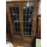 An oak bookcase with 2 leaded glazed doors above double door cupboard below