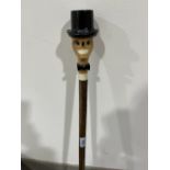 A hazel walking stick, the pommel carved as a grinning skull in top hat with glass eyes. 53' long