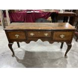 An antique oak and mahogany dresser base, with three drawers and shaped apron, raised on cabriole