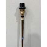 A hazel walking stick, the pommel carved as a grinning skull in top hat with glass eyes. 53' long