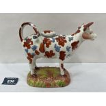 A 19th century Staffordshire cow creamer painted with flowerheads in red ochre and blue. 7' long