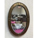 An Arts and Crafts oval mirror with planished brass frame and bevelled plate. 24' high