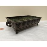 A 19th century Chinese bronze rectilinear jardiniere with chimera head handles, raised on bracket