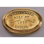 An oval brass snuff box, dated 1910, stamped with clasped hands, tobacco pipes and, in printer's